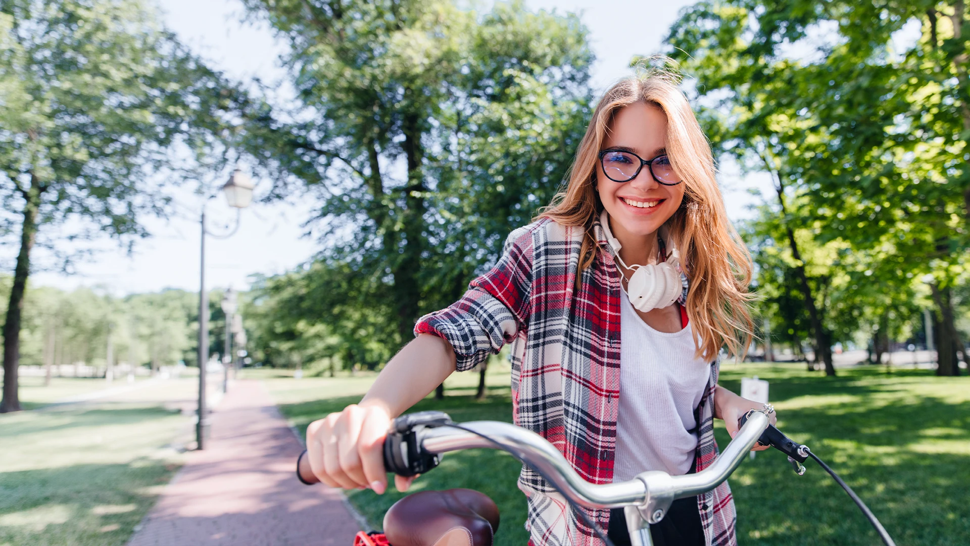 Smiling woman with glasses riding a bicycle through a sunlit park